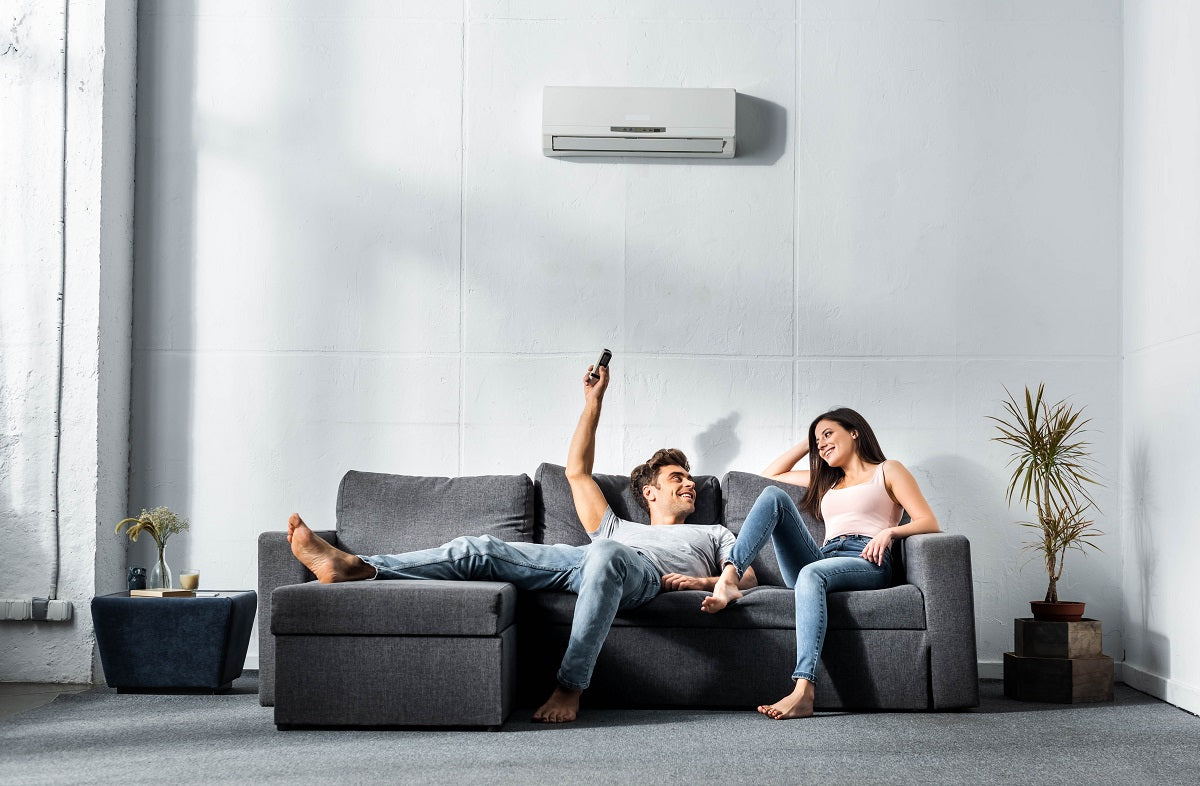 handsome boyfriend switching on air conditioner and looking at smiling girlfriend