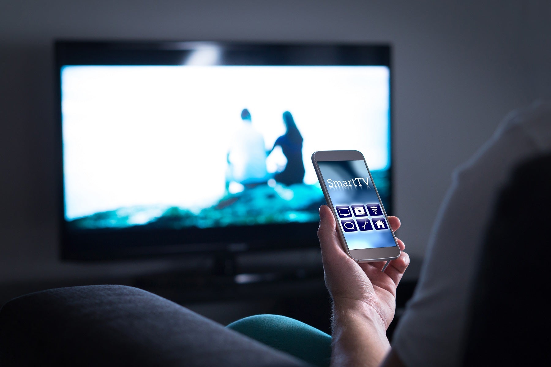 Man watching television and using smart tv remote control app on mobile